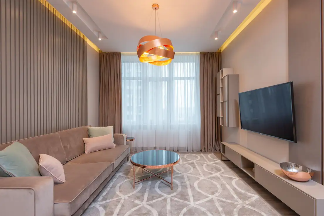 A sofa about two-thirds the length of the wall behind it, with a round coffee table and rug in a small living room facing a wall-mounted TV
