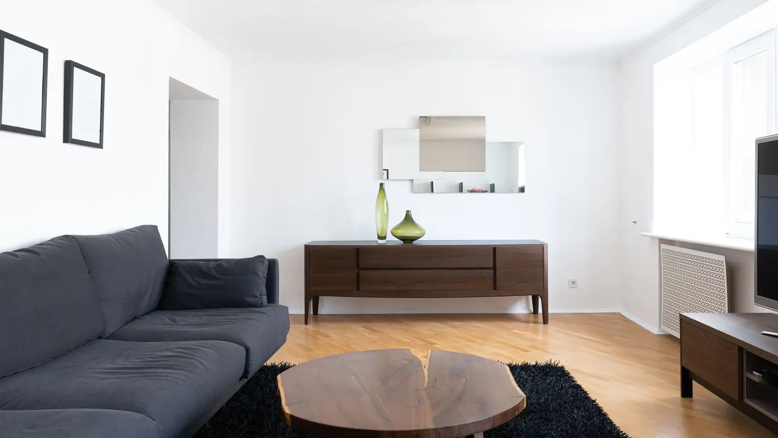 A low-profile dark sofa in a small apartment living room with an open sightline to the kitchen
