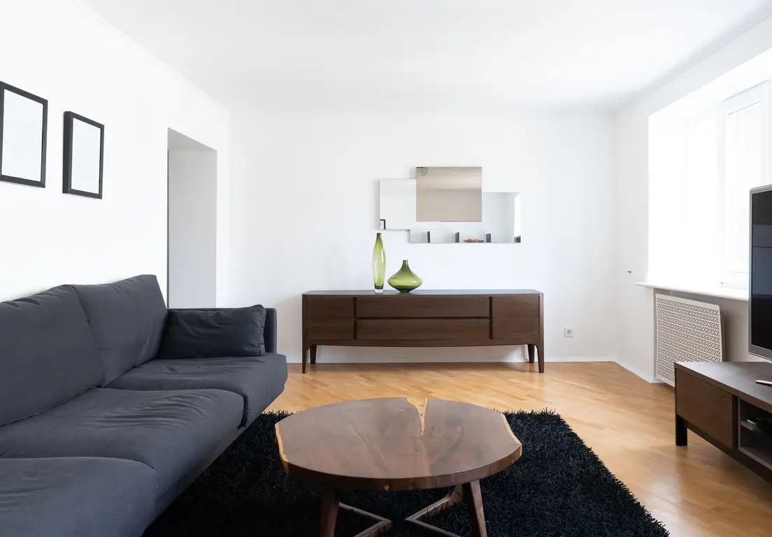 A low-profile dark sofa in a small apartment living room with an open sightline to the kitchen