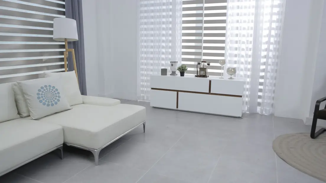 A stark white modern living room with a white sectional and gray tile floor, the cool look organic modern style warms up