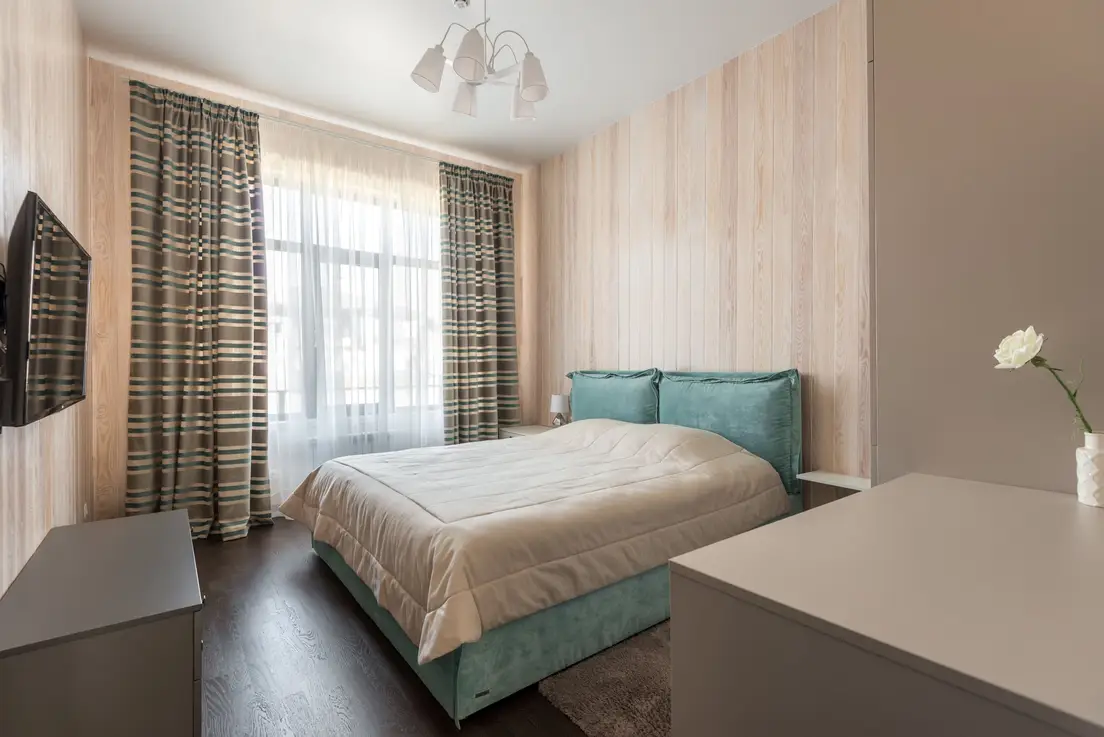 A small apartment bedroom with a low platform storage bed against a curtained window