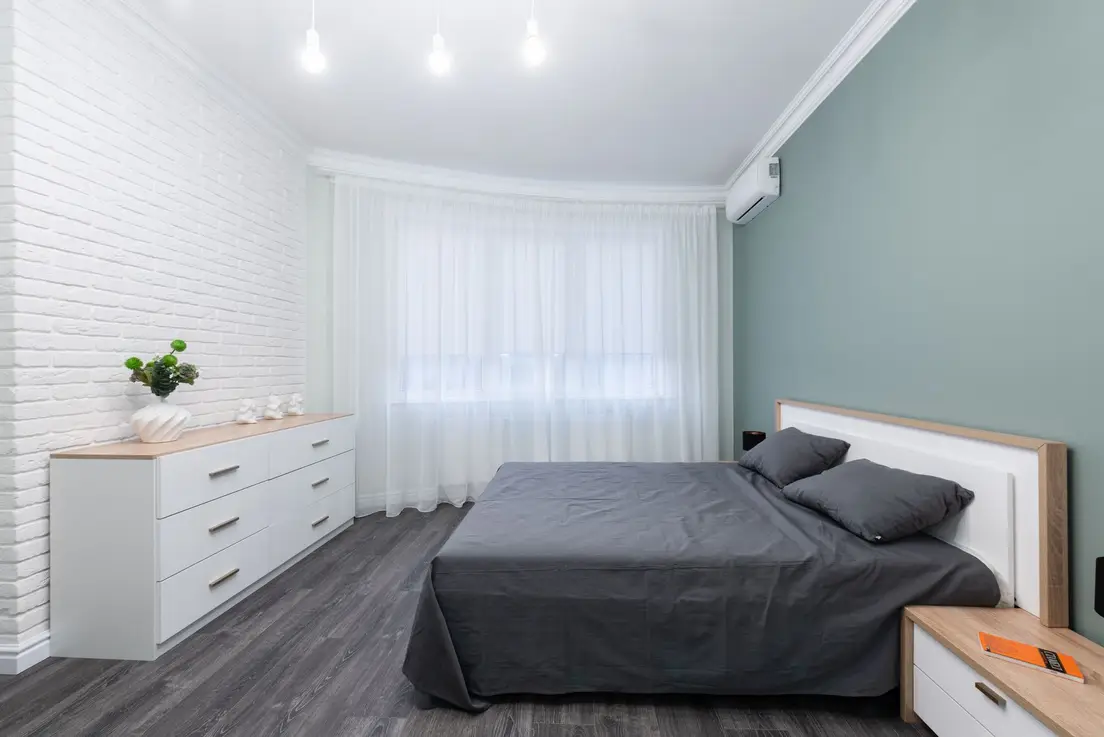 A small bedroom with a storage dresser against a sage green accent wall