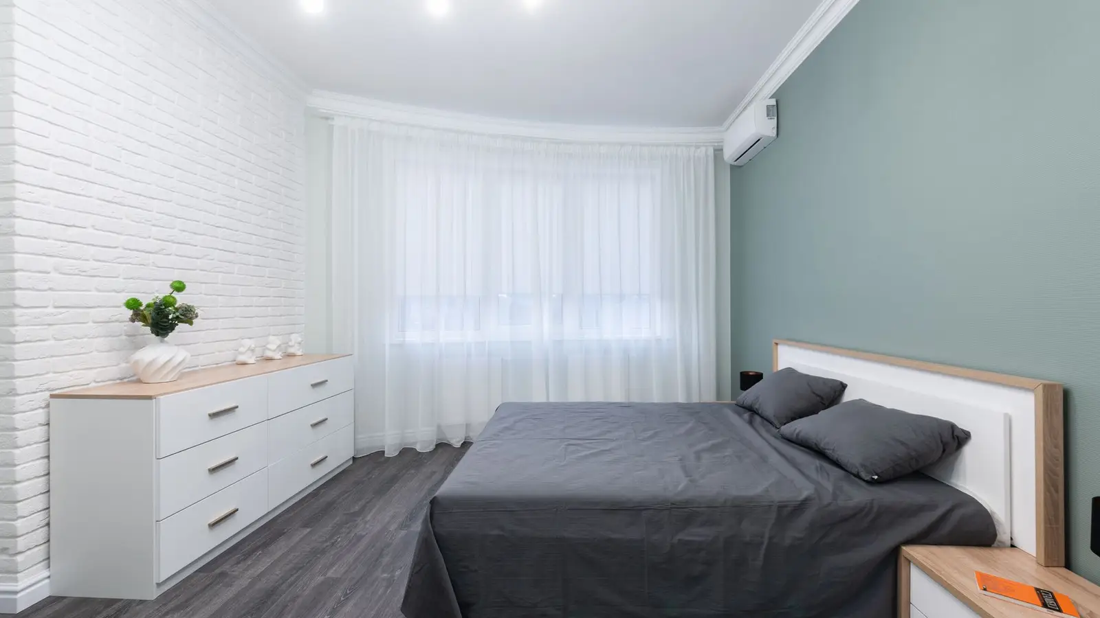 A small bedroom with a storage dresser against a sage green accent wall