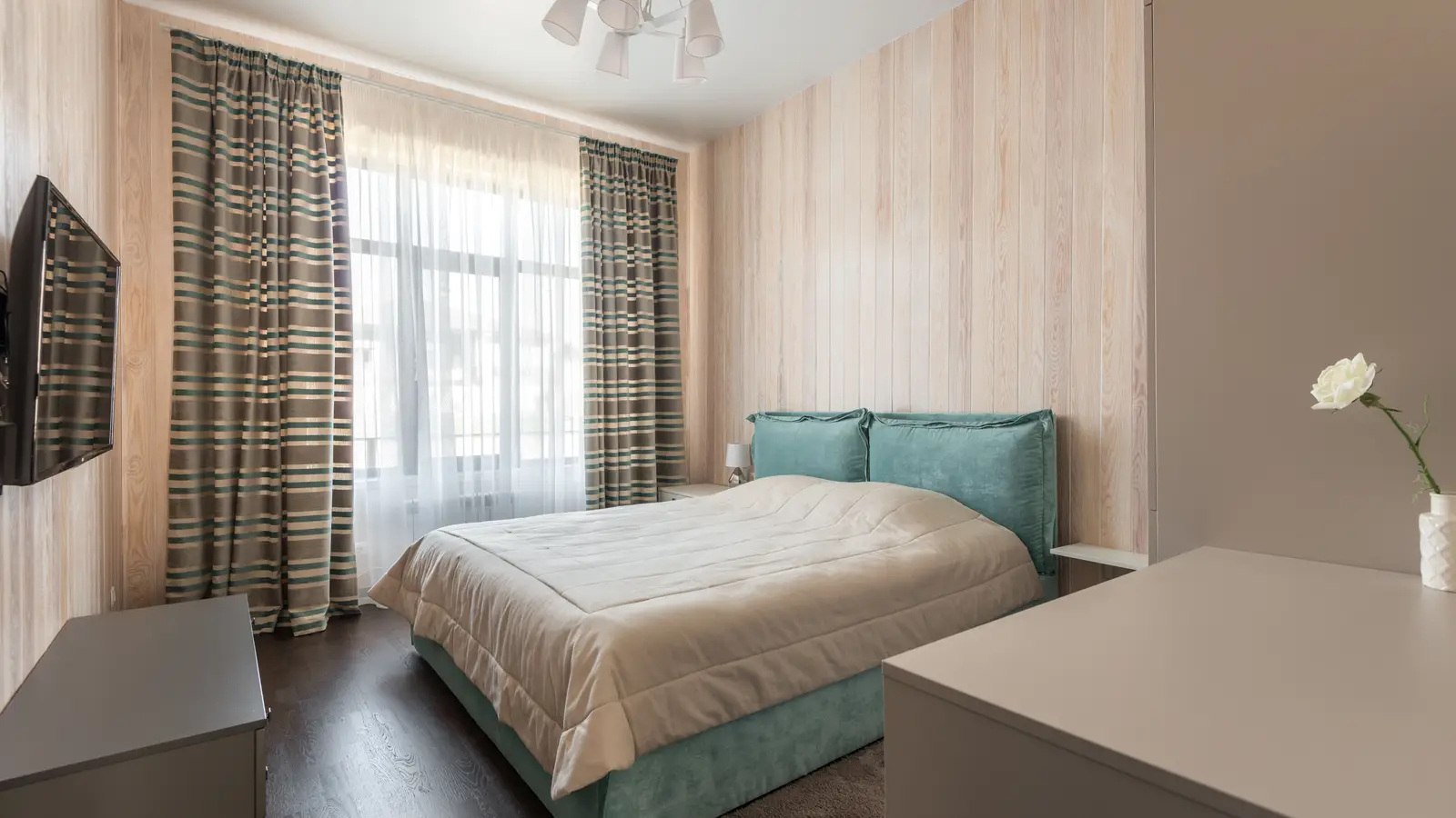 A small apartment bedroom with a low platform storage bed against a curtained window