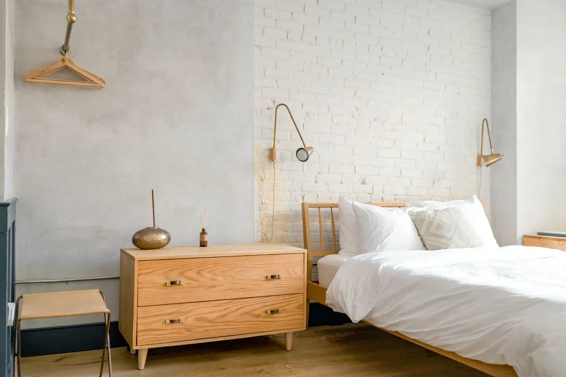 A warm wood dresser with a reed diffuser against a whitewashed brick wall
