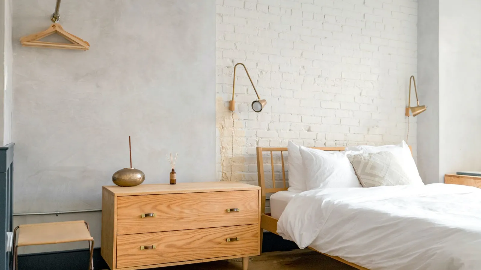 A warm wood dresser with a reed diffuser against a whitewashed brick wall
