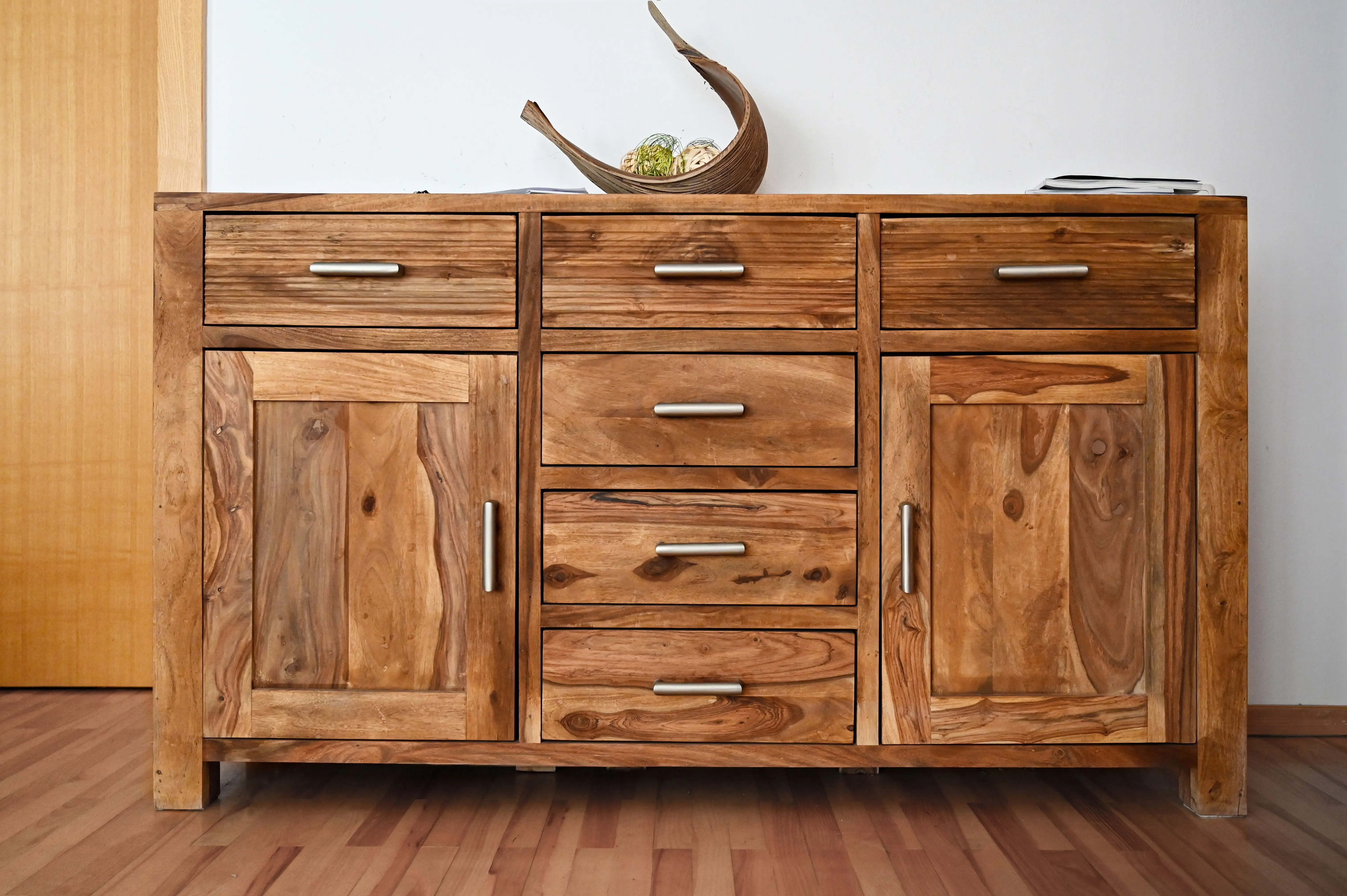 A closed wooden storage cabinet with drawers and natural wood grain for a living room console