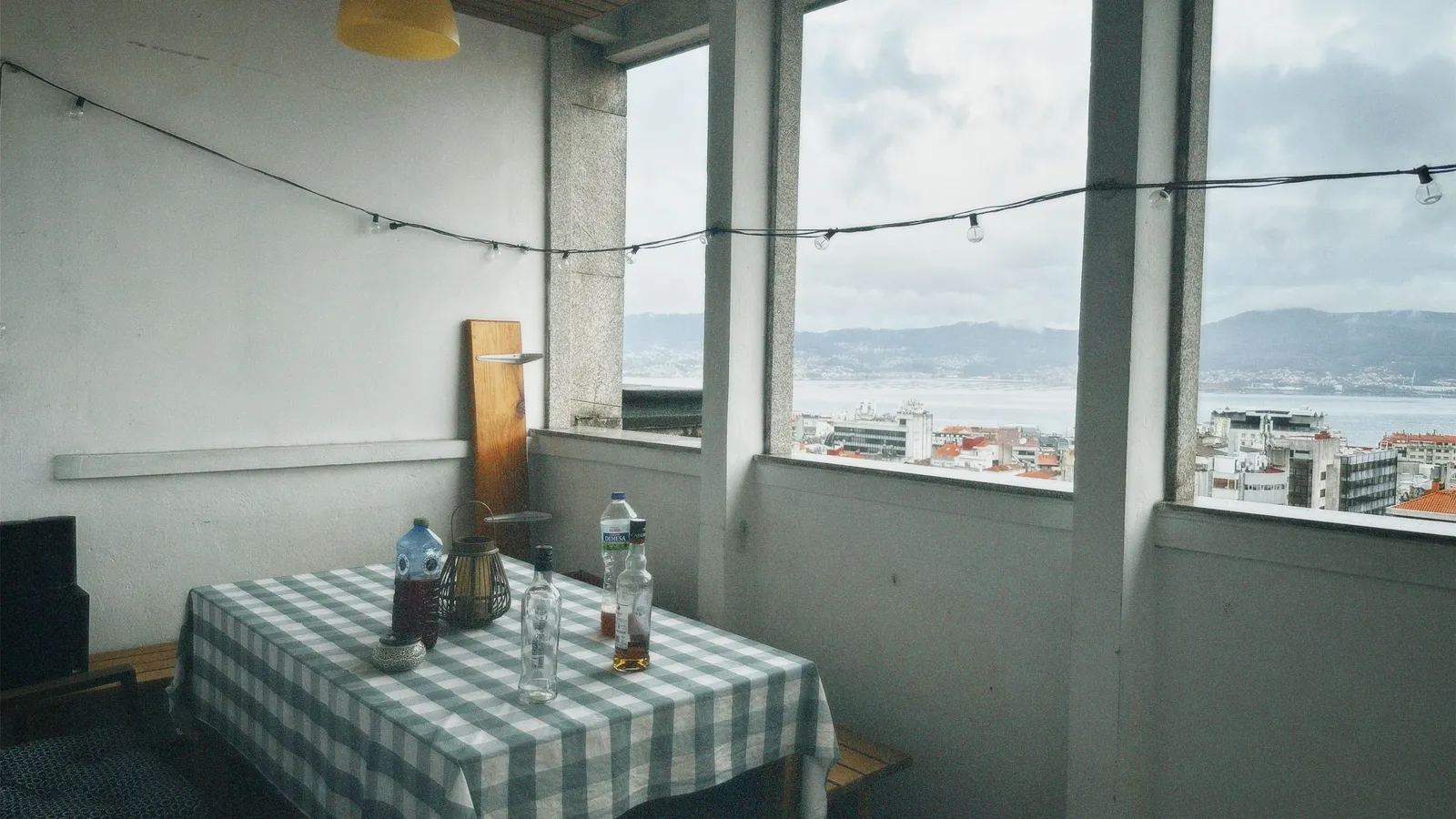 String lights strung across a rooftop balcony dining area at dusk with a city view