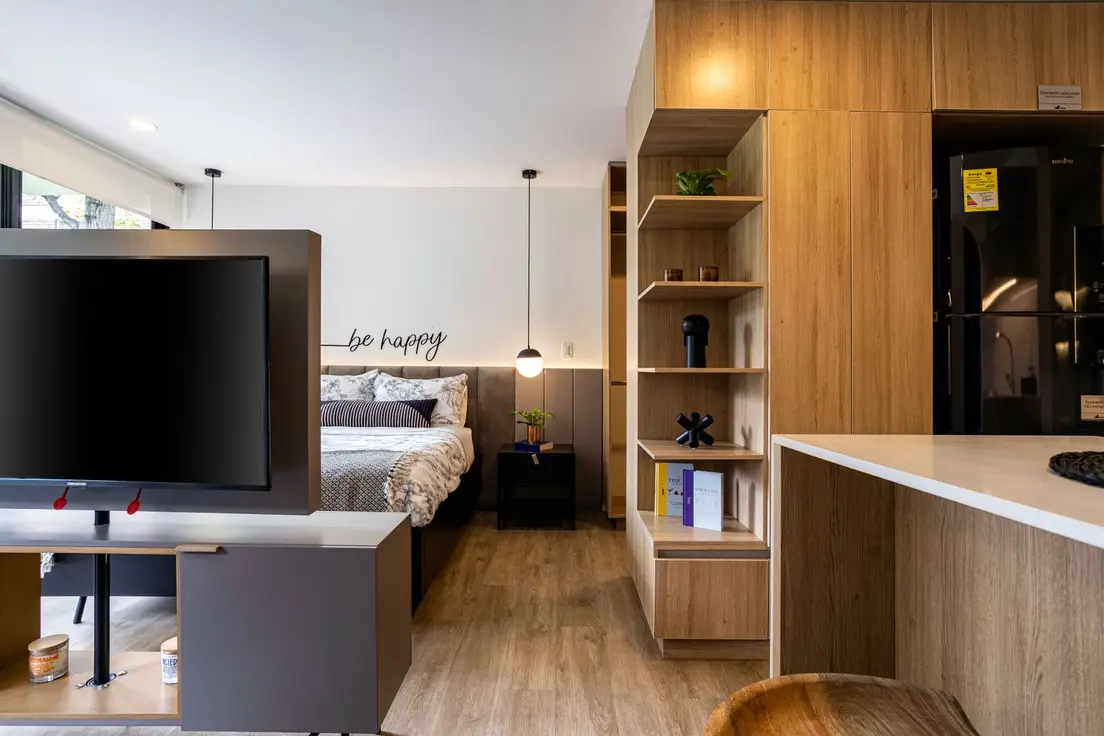 A furnished studio apartment with a shelving console dividing the bed area from the living space