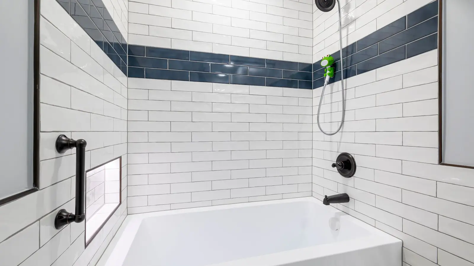 A small bathroom shower wall with a white subway tile pattern and navy accent stripe