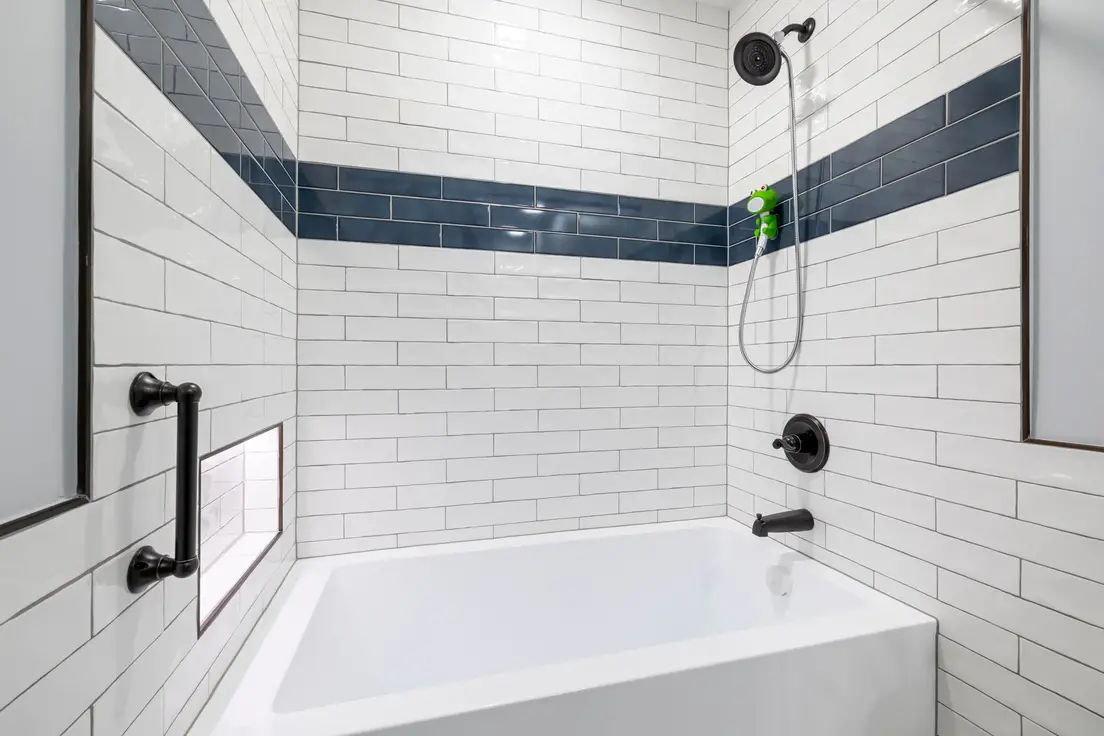 A small bathroom shower wall with a white subway tile pattern and navy accent stripe