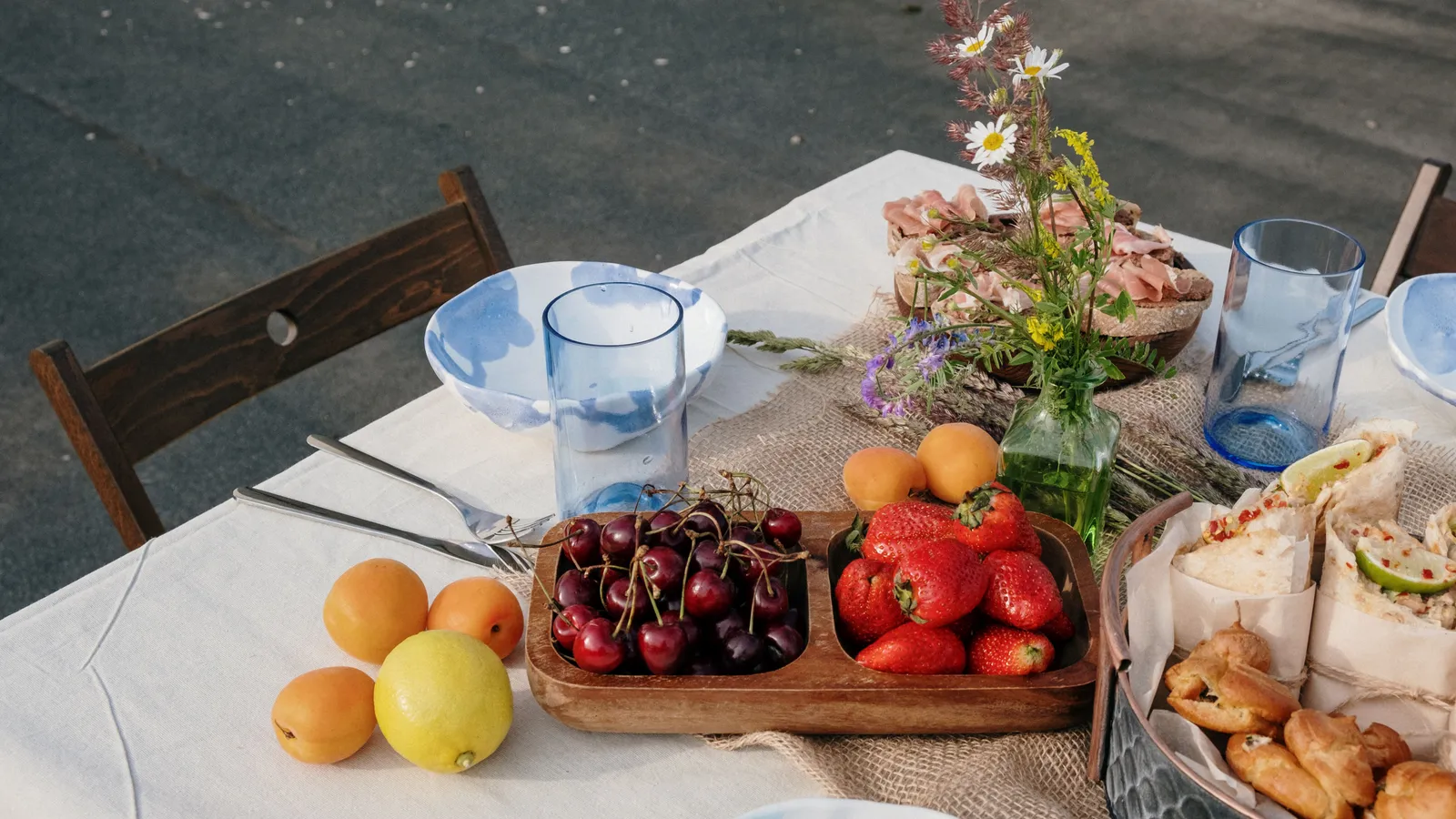 An outdoor party table set with a linen runner, fresh fruit, and flowers
