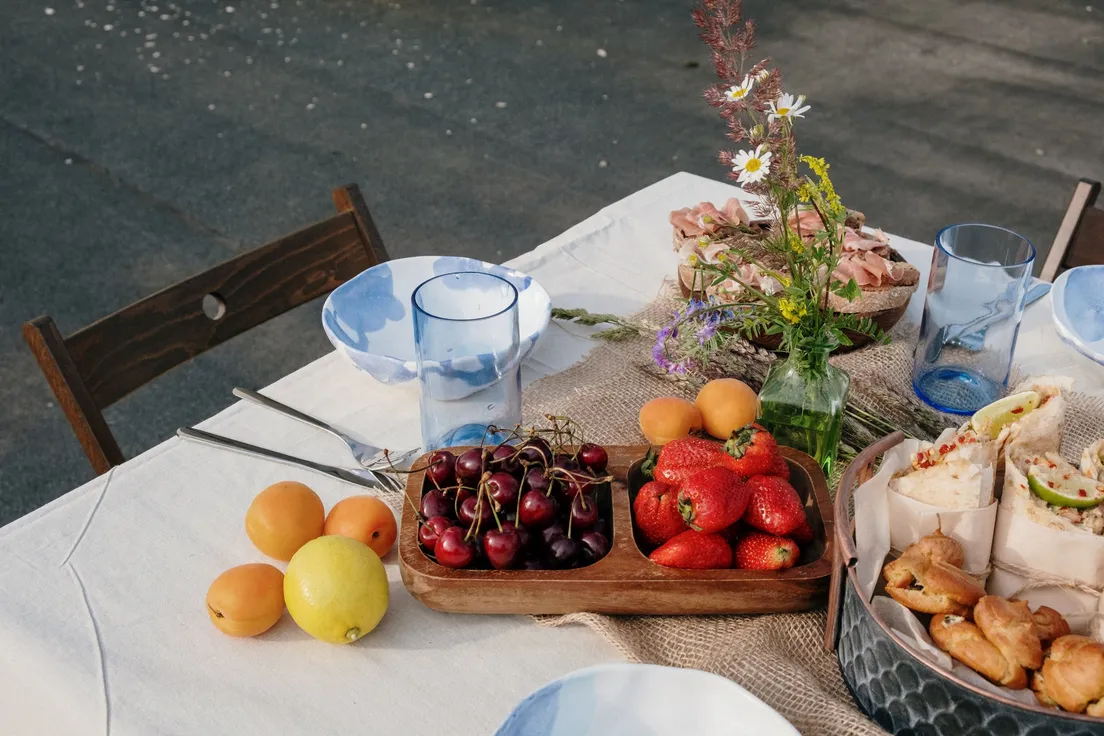 An outdoor party table set with a linen runner, fresh fruit, and flowers