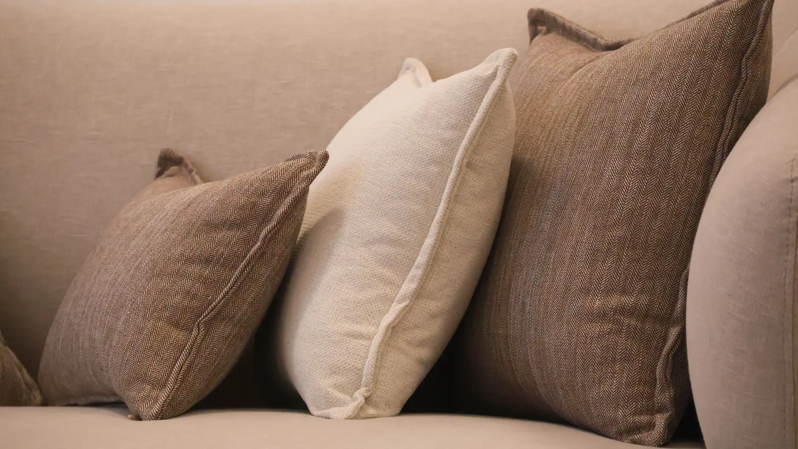 Neutral linen and herringbone throw pillows layered on a beige minimalist sofa