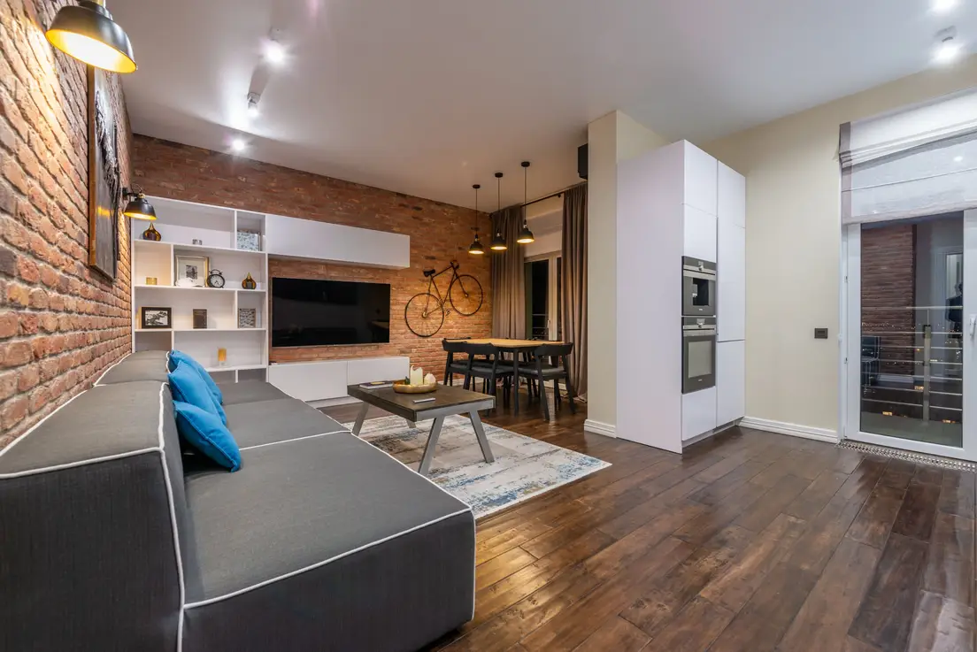A wall-mounted TV against an exposed brick accent wall next to white built-in shelving