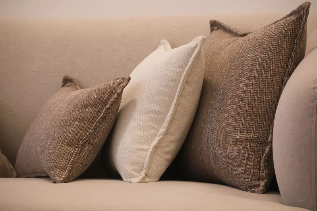 Neutral linen and herringbone throw pillows layered on a beige minimalist sofa