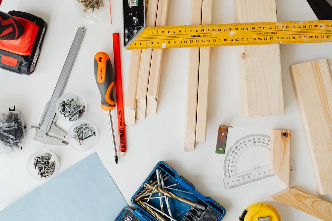 Carpentry tools, wood strips, screws, and a tape measure laid out on a workbench for a temporary wall build
