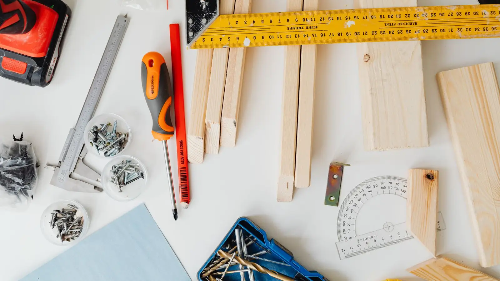 Carpentry tools, wood strips, screws, and a tape measure laid out on a workbench for a temporary wall build