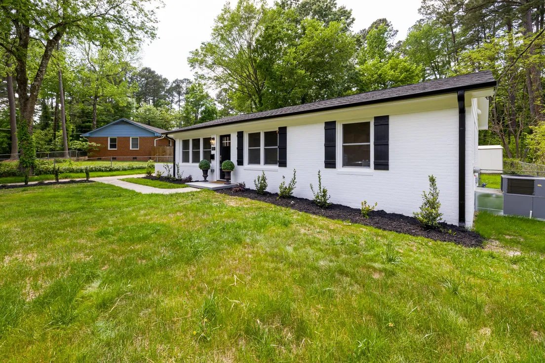A white ranch house exterior with black trim repeated across the shutters, door, and hardware