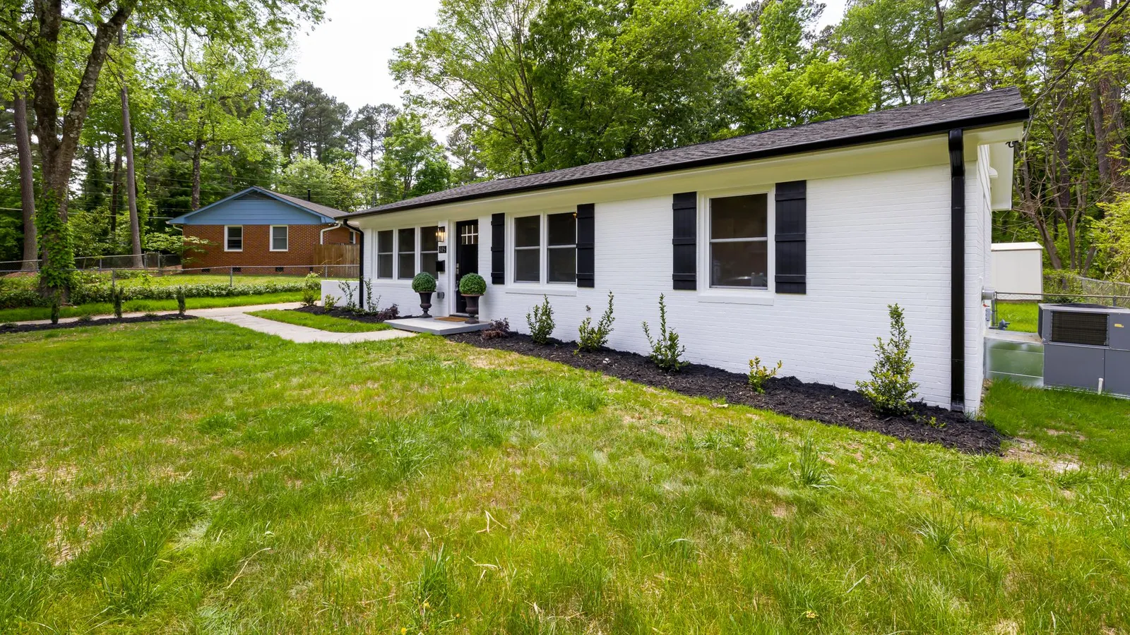 A white ranch house exterior with black trim repeated across the shutters, door, and hardware
