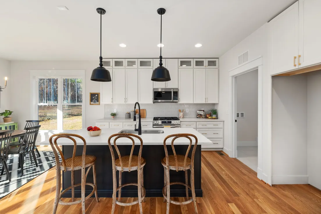 A two-tone modern farmhouse kitchen with white upper cabinets, a dark island, and black pendant lights