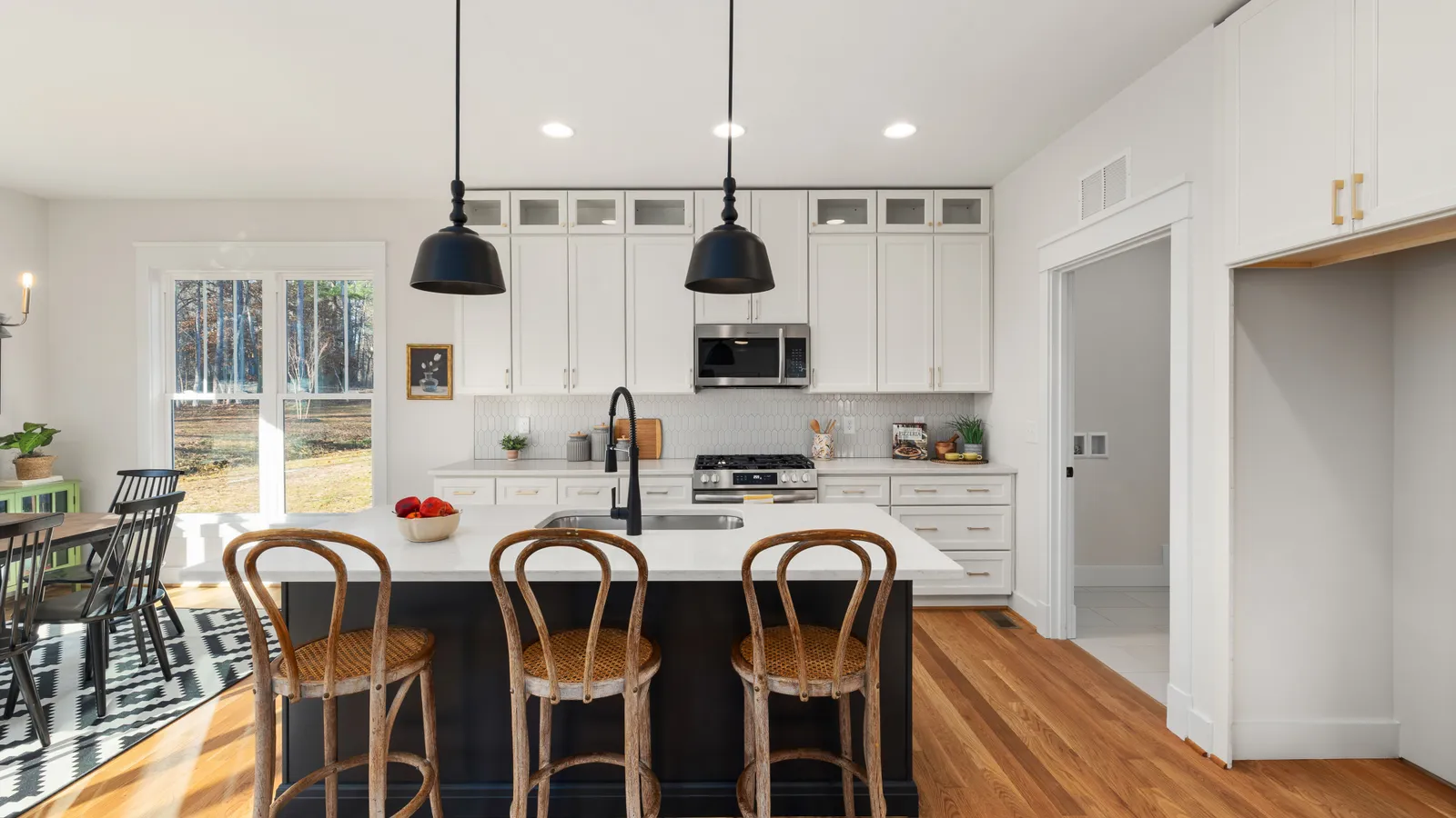 A two-tone modern farmhouse kitchen with white upper cabinets, a dark island, and black pendant lights
