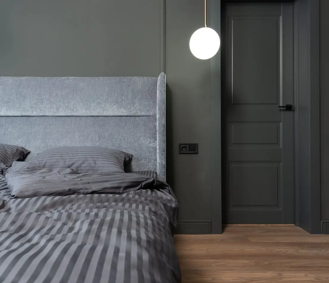 A grey upholstered wingback headboard against a deep olive wall with striped grey bedding