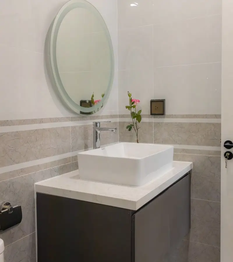 A small bathroom with a dark floating vanity and round mirror mounted above it