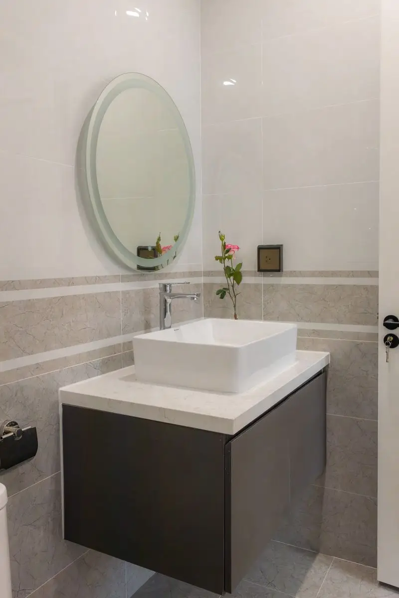 A small bathroom with a dark floating vanity and round mirror mounted above it