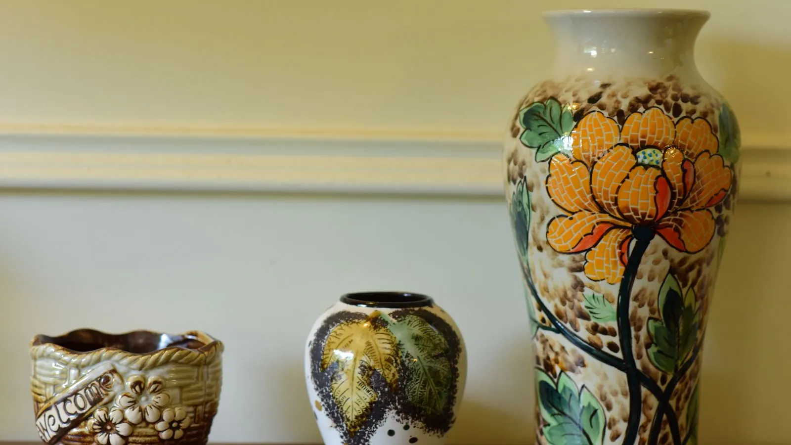 Three colorful hand-painted ceramic vases grouped on a wooden shelf