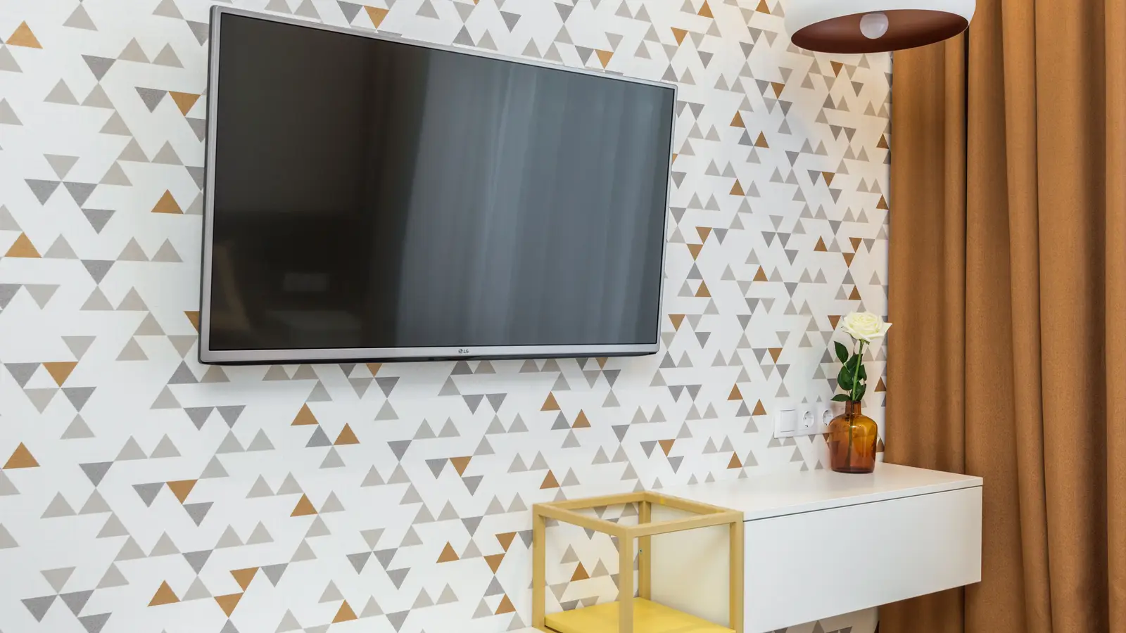 A wall-mounted TV against a geometric triangle-print peel-and-stick wallpaper accent wall