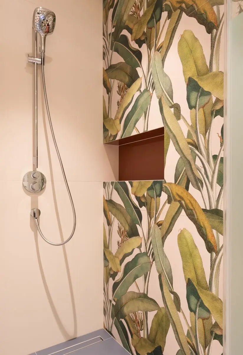 A bold botanical leaf-print wallpaper on a bathroom accent wall beside a shower fixture