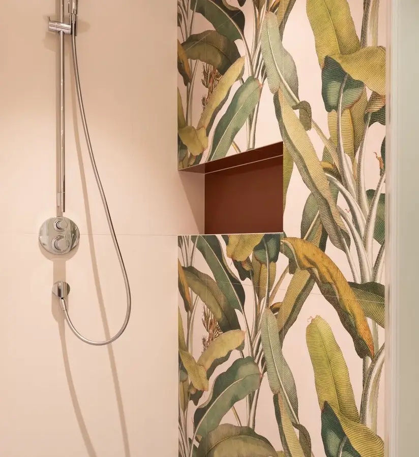 A bold botanical leaf-print wallpaper on a bathroom accent wall beside a shower fixture