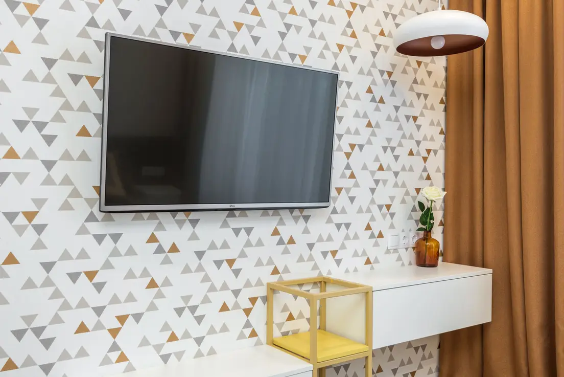 A wall-mounted TV against a geometric triangle-print peel-and-stick wallpaper accent wall