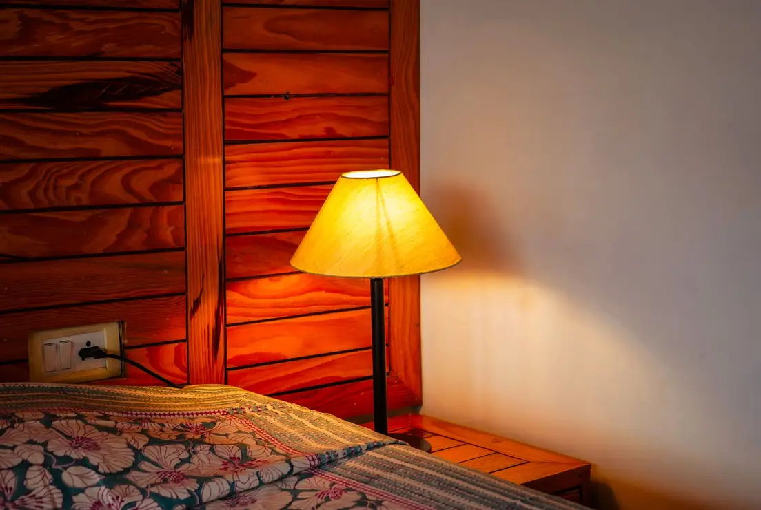 A warm 2700K bedside lamp glowing against a wood plank wall in a mens bedroom