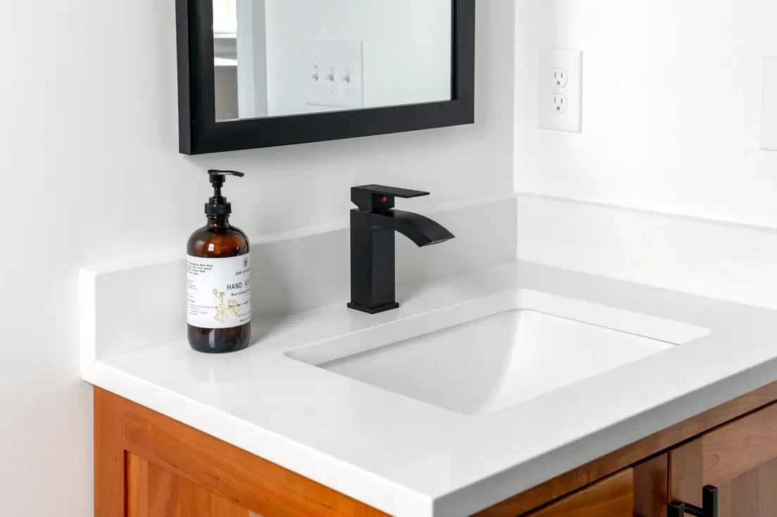 A simple white bathroom countertop with a matte black faucet and framed mirror