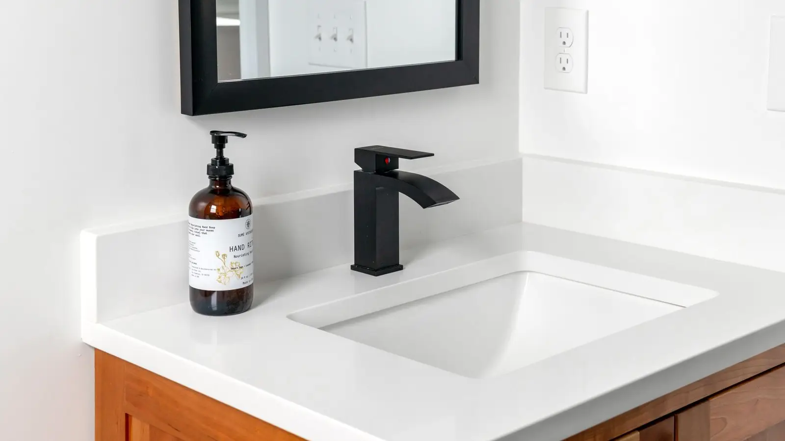 A simple white bathroom countertop with a matte black faucet and framed mirror