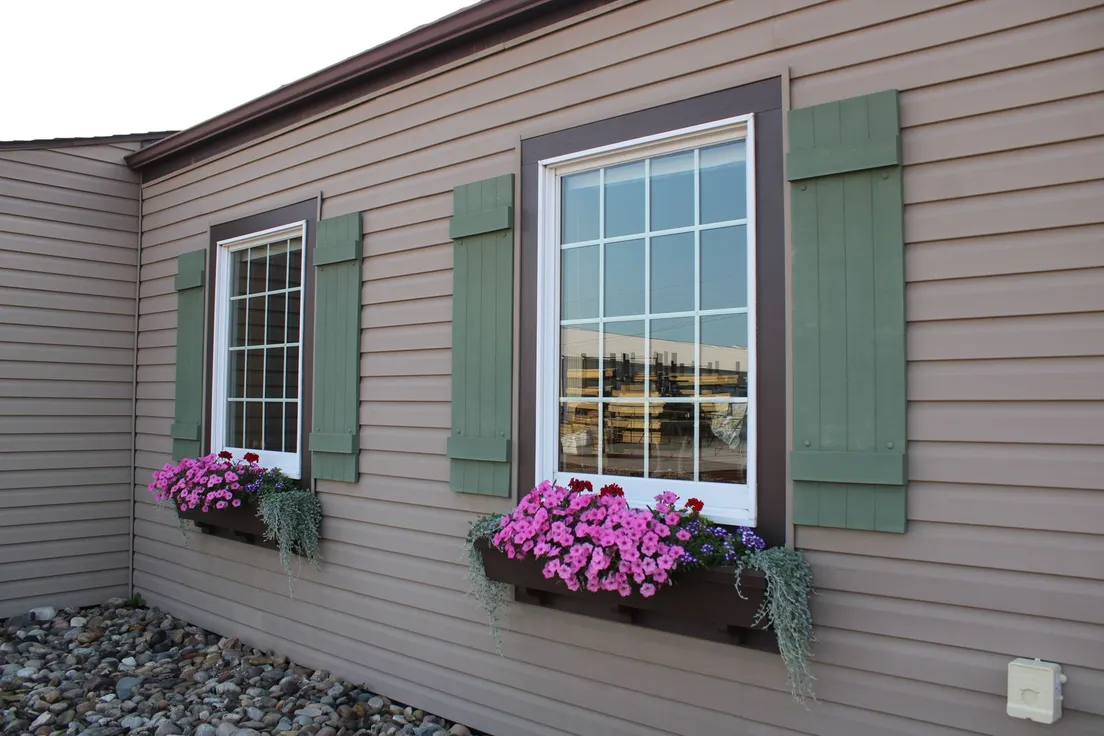 Vinyl-sided house windows with green shutters and full window boxes of pink flowers