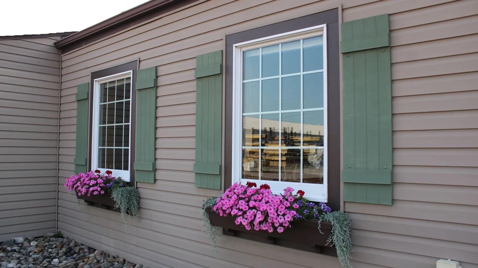 Vinyl-sided house windows with green shutters and full window boxes of pink flowers