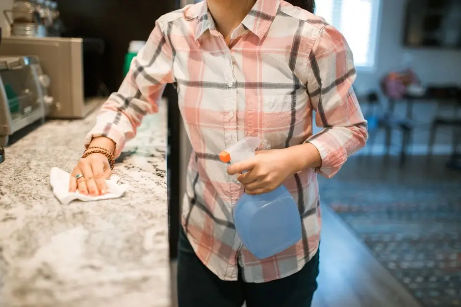 A person wiping down a kitchen counter with a cloth and spray cleaner