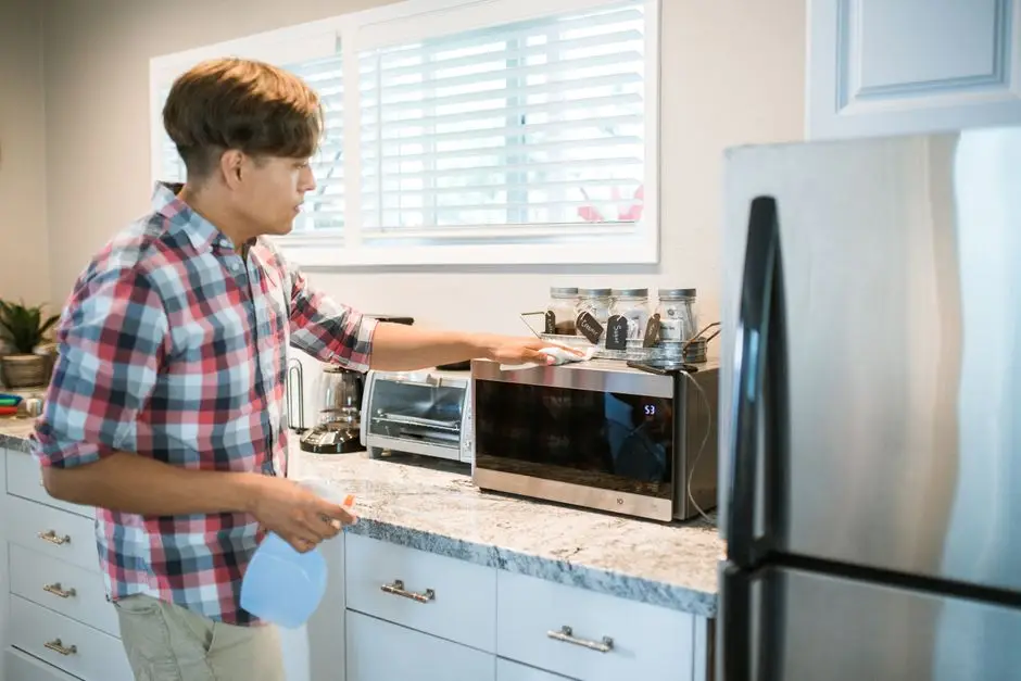 A man wiping down the exterior of a countertop oven in a kitchen