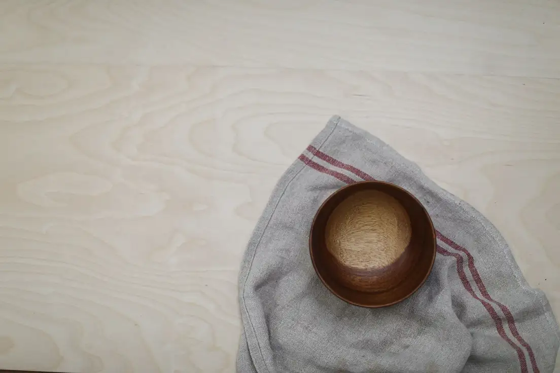 A turned wooden bowl on a natural linen towel over a light birch wood surface, organic modern materials up close
