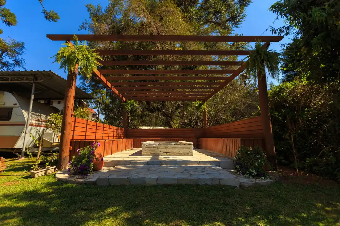 A wood-framed freestanding patio cover with exposed rafters in a backyard