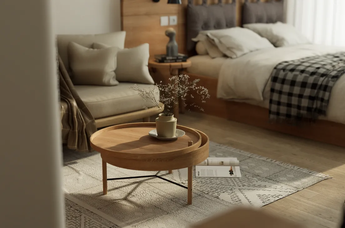 A warm wood round tray table with a small vase beside a linen sofa in a Scandinavian-style bedroom