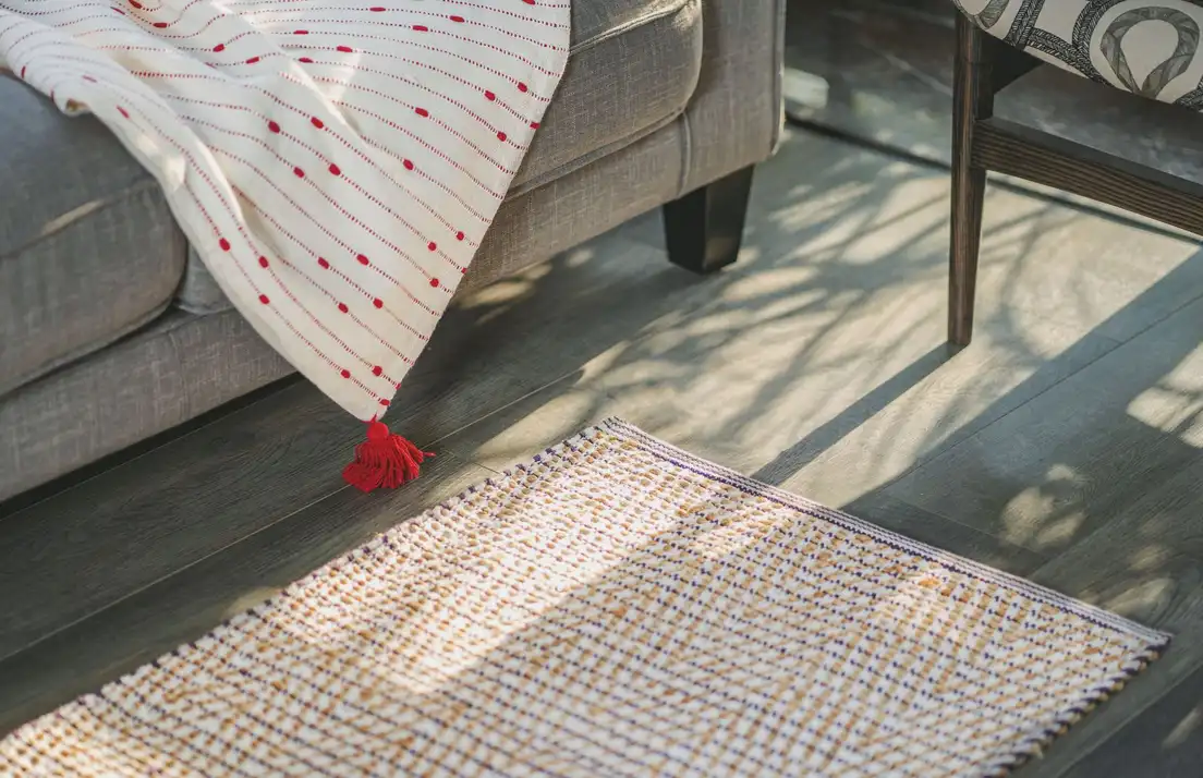 A handwoven textured rug on a wood floor beside a sofa with a cream throw, layered organic modern texture