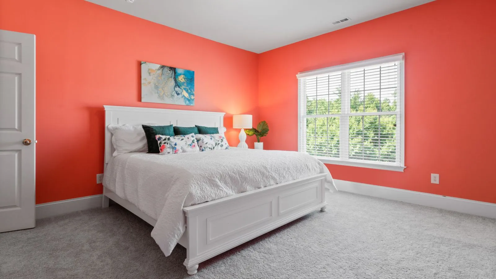 A bedroom with a bright coral accent wall behind the bed and calm white bedding, showing dopamine decor color zoning